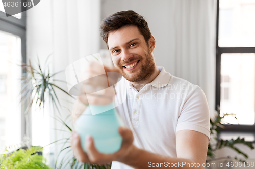 Image of man spraying houseplants with water at home