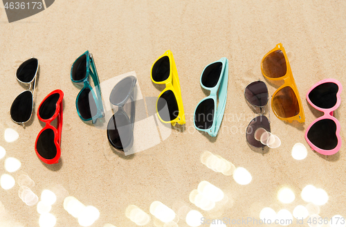 Image of different sunglasses on beach sand