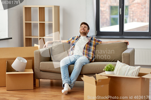 Image of happy man with boxes sitting on sofa at new home