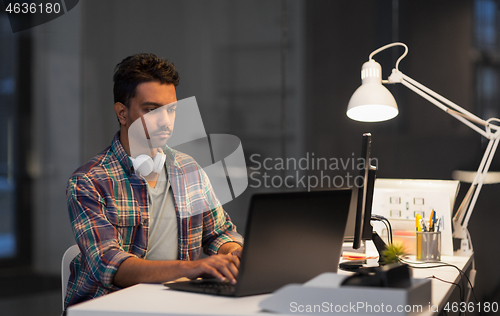 Image of creative man with laptop working at night office