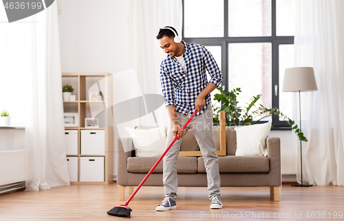 Image of man in headphones with broom cleaning at home