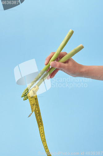 Image of Female\'s hand with asparagus sticks is taking measure tape.