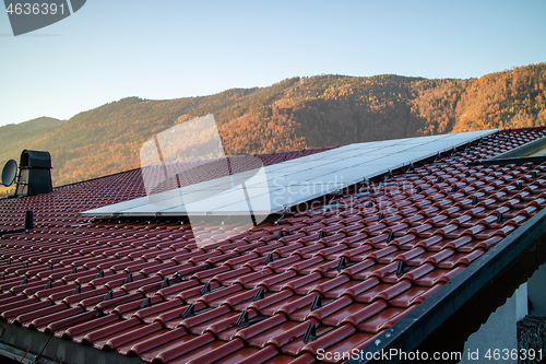 Image of Tile roof with solar panel on a mountain background, Austria.