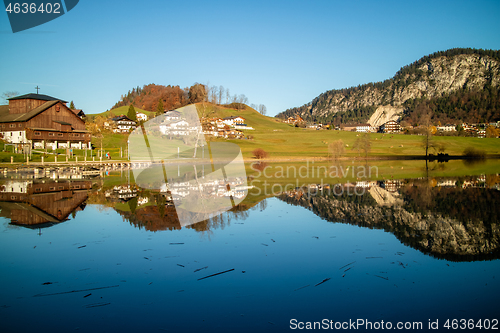 Image of Autumn countryside landscape with reflection of houses in blue lake.