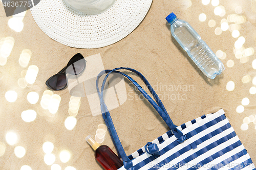 Image of beach bag, sunscreen, sunglasses and hat on sand