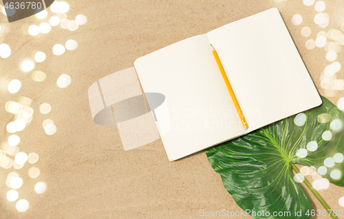 Image of notebook with pencil and leaf on beach sand