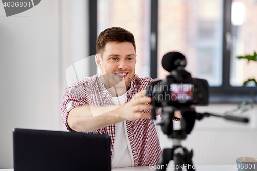 Image of male video blogger adjusting camera at home office