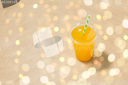 Image of cup of orange juice with straw on beach sand