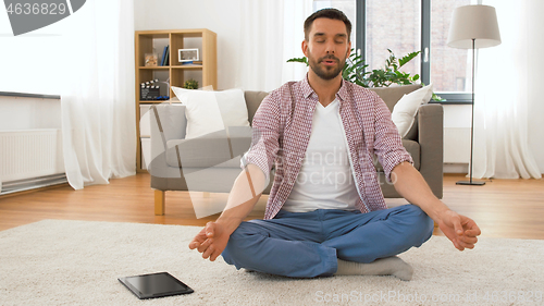 Image of man with tablet computer meditating at home