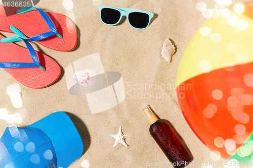 Image of cap, flip flops and shades and beach ball on sand