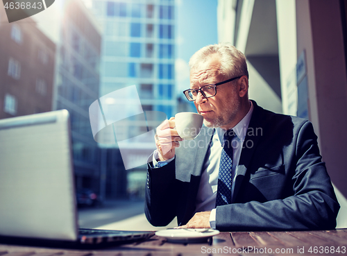 Image of senior businessman with laptop drinking coffee