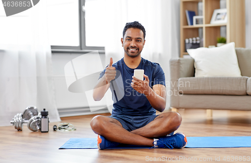 Image of indian man with smartphone on exercise mat at home