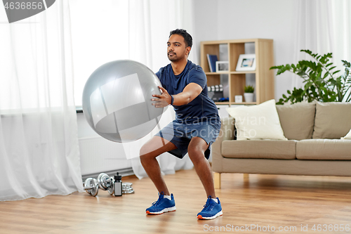 Image of man exercising and doing squats with ball at home