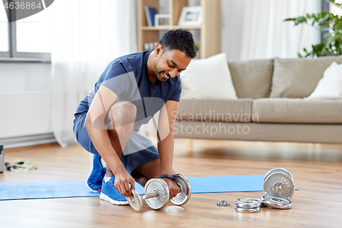 Image of smiling indian man assembling dumbbells at home