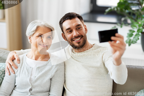 Image of senior mother with adult son taking selfie at home