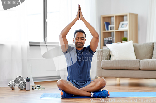 Image of indian man meditating in lotus pose at home