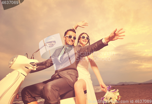 Image of just married couple on the beach ride white scooter