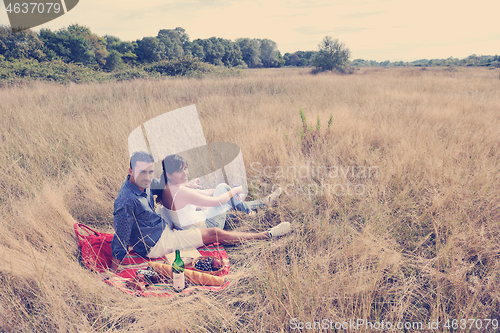 Image of happy couple enjoying countryside picnic in long grass