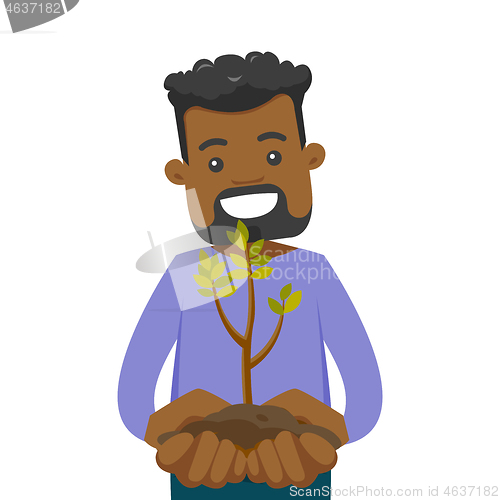 Image of African-american man holding green plant in soil.