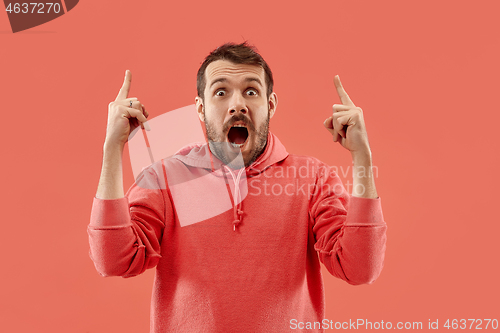 Image of The young attractive man looking suprised isolated on coral