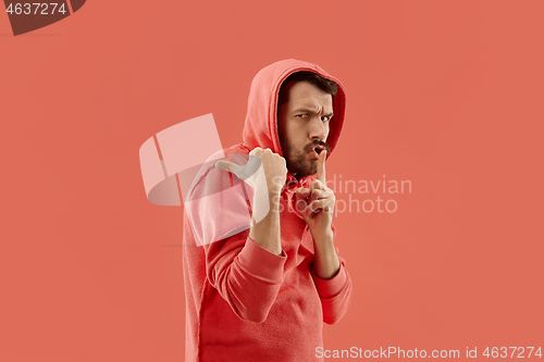 Image of The young man whispering a secret behind her hand over coral background