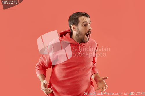 Image of The young attractive man looking suprised isolated on coral