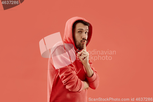 Image of The young man whispering a secret behind her hand over coral background