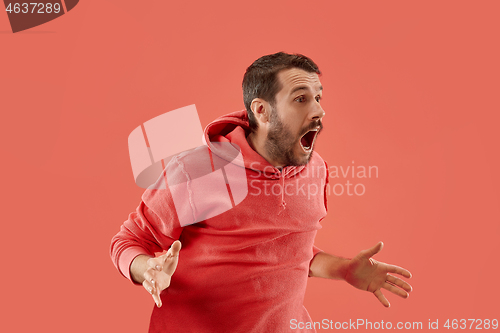 Image of The young attractive man looking suprised isolated on coral