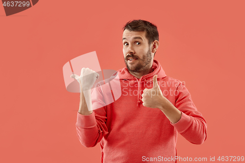 Image of The young attractive man looking suprised isolated on coral