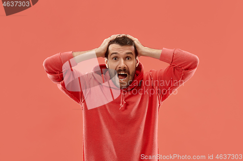 Image of The young attractive man looking suprised isolated on coral