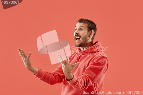 Image of The young attractive man looking suprised isolated on coral