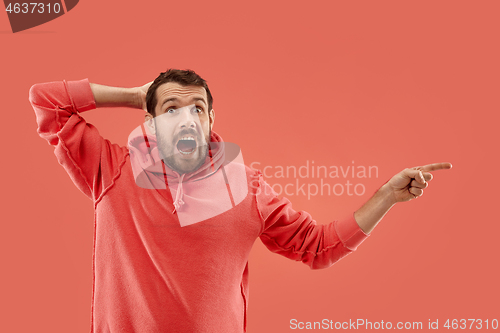 Image of The young attractive man looking suprised isolated on coral