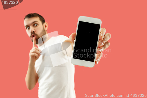 Image of Young handsome man showing smartphone screen isolated on coral background in shock with a surprise face