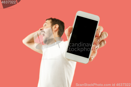 Image of Young handsome man showing smartphone screen isolated on coral background in shock with a surprise face