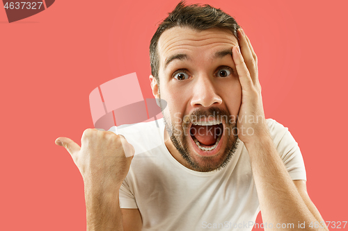 Image of The young attractive man looking suprised isolated on coral