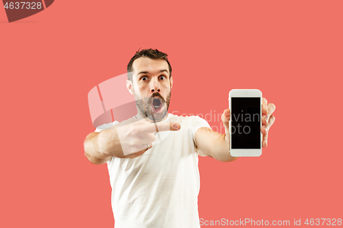 Image of Young handsome man showing smartphone screen isolated on coral background in shock with a surprise face