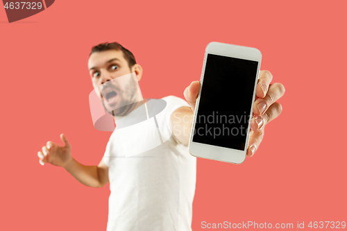 Image of Young handsome man showing smartphone screen isolated on coral background in shock with a surprise face