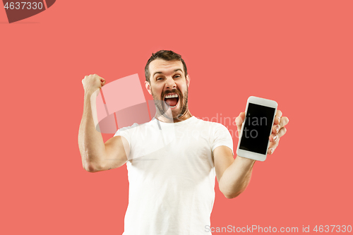 Image of Young handsome man showing smartphone screen isolated on coral background in shock with a surprise face