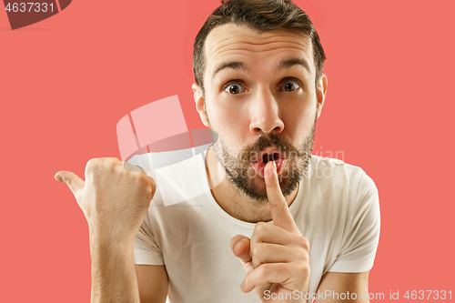 Image of The young man whispering a secret behind her hand over coral background