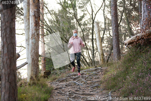 Image of Corona virus, or Covid-19, is spreading all over the world. Portrait of caucasian sporty woman wearing a medical protection face mask while running in nature.