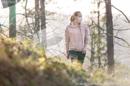 Image of Corona virus, or Covid-19, is spreading all over the world. Portrait of caucasian sporty woman wearing a medical protection face mask while walking in the forest. Corona virus.