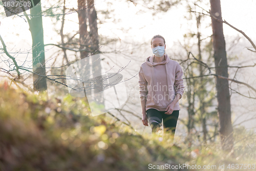 Image of Corona virus, or Covid-19, is spreading all over the world. Portrait of caucasian sporty woman wearing a medical protection face mask while walking in the forest. Corona virus.