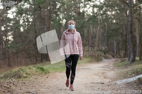 Image of Corona virus, or Covid-19, is spreading all over the world. Portrait of caucasian sporty woman wearing a medical protection face mask while walking in the forest. Corona virus.