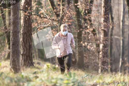 Image of Corona virus, or Covid-19, is spreading all over the world. Portrait of caucasian sporty woman wearing a medical protection face mask while running in nature.