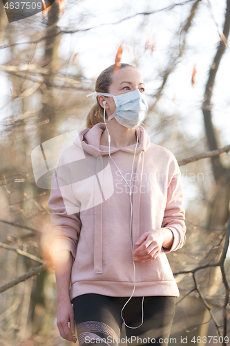 Image of Portrait of caucasian sporty woman wearing medical protection face mask while walking in park, relaxing and listening to music. Corona virus, or Covid-19, is spreading all over the world