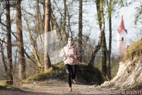 Image of Corona virus, or Covid-19, is spreading all over the world. Portrait of caucasian sporty woman wearing a medical protection face mask while running in nature.