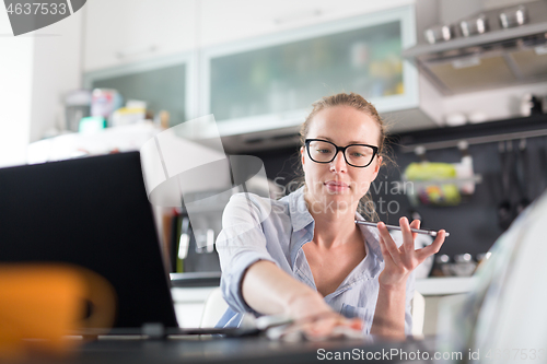 Image of Stay at home and social distancing. Woman in her casual home clothing working remotly from her kitchen dining table in the morning. Video chatting with friend, family or business clients or partners