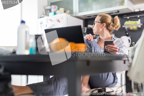 Image of Stay at home and social distancing. Woman in her casual home clothing working remotly from kitchen dining table. Video chatting using social media with friend, family, business clients or partners