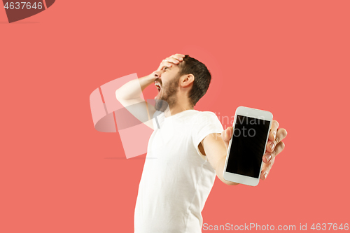 Image of Young handsome man showing smartphone screen isolated on coral background in shock with a surprise face