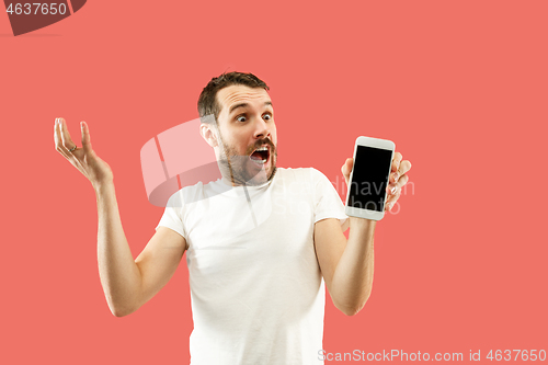 Image of Young handsome man showing smartphone screen isolated on coral background in shock with a surprise face